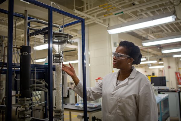 Teaching assistant professor Uzoma Monye inspects the liquid-liquid extraction column that students use to investigate the removal of t-butyl alcohol from mineral oil.