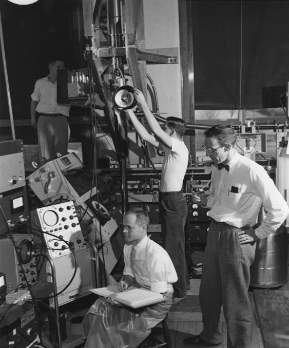 教授约翰·惠特利(坐着),他在1965年将达到世界纪录then-lowest temperature— 0.003度以上绝对zero—低温物理实验室中的数据,物理1957年的旧建筑的地下室里。站在惠特利是狄龙Mapother教授。背景的研究生托马斯Estle(中心)和霍华德·哈特(左)。这张照片最初发表在伊利诺斯州校友新闻,36卷,第3号(1957年4月)。图片由伊利诺斯州大学的校友会。