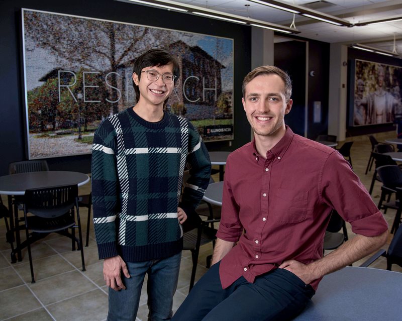 Graduate students Seonghwan Kim, left, and Kastan Day post for a picture near a table and chairs within the National Center for Supercomupting Applications building.